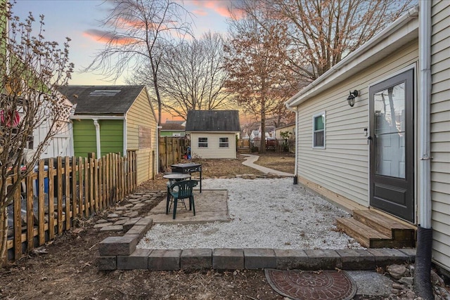 patio terrace at dusk featuring a storage unit, an outbuilding, a fenced backyard, and entry steps