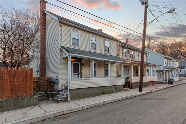 townhome / multi-family property featuring a residential view, a porch, a chimney, and fence