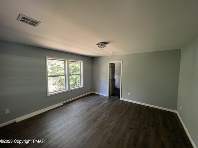 empty room featuring dark wood-style floors, visible vents, and baseboards