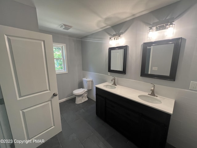 bathroom featuring toilet, double vanity, visible vents, and a sink