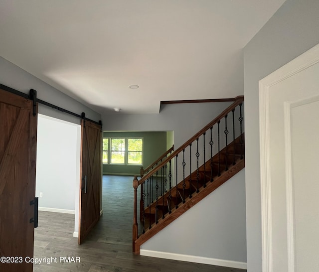 stairway featuring a barn door, baseboards, and wood finished floors