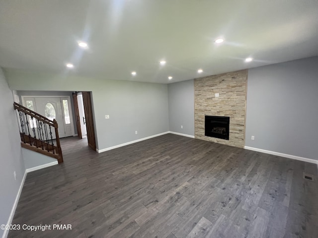 unfurnished living room featuring dark wood-type flooring, visible vents, a stone fireplace, and baseboards