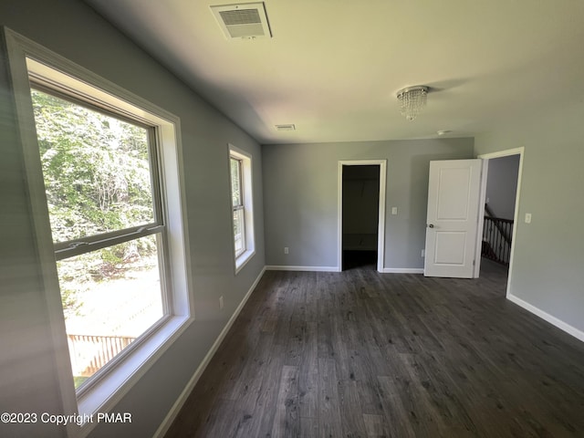 unfurnished room with dark wood-type flooring, a wealth of natural light, visible vents, and baseboards