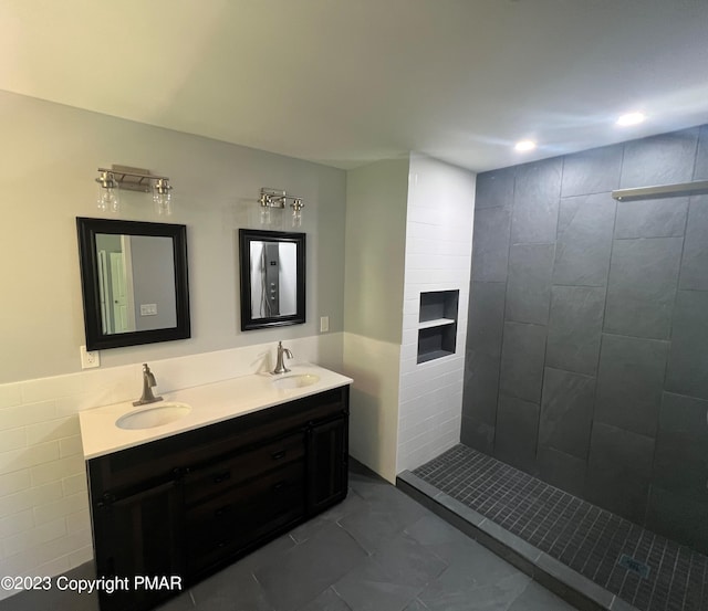 bathroom featuring marble finish floor, a sink, a tile shower, and double vanity