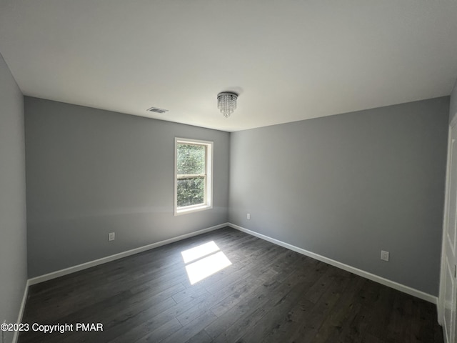 unfurnished room with dark wood-style floors, visible vents, and baseboards