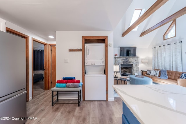 kitchen with light wood finished floors, lofted ceiling with beams, a fireplace, stacked washing maching and dryer, and freestanding refrigerator