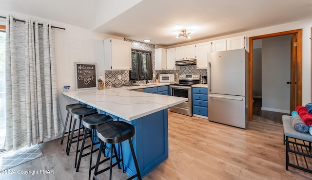 kitchen featuring a peninsula, stainless steel appliances, white cabinets, under cabinet range hood, and backsplash