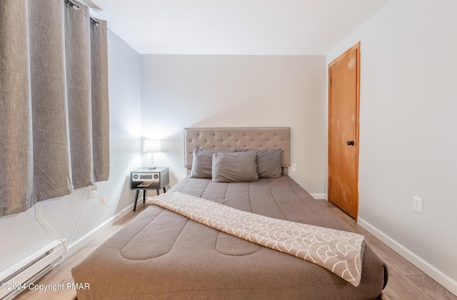 bedroom with baseboards, a baseboard heating unit, and light wood-style floors