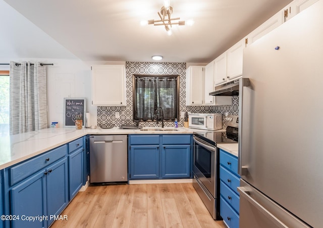 kitchen featuring under cabinet range hood, appliances with stainless steel finishes, white cabinetry, blue cabinets, and a sink