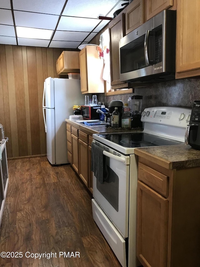 kitchen with dark wood-type flooring, white appliances, a paneled ceiling, and wood walls