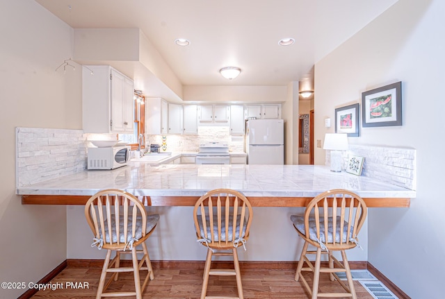 kitchen featuring built in desk, white cabinetry, sink, kitchen peninsula, and white appliances