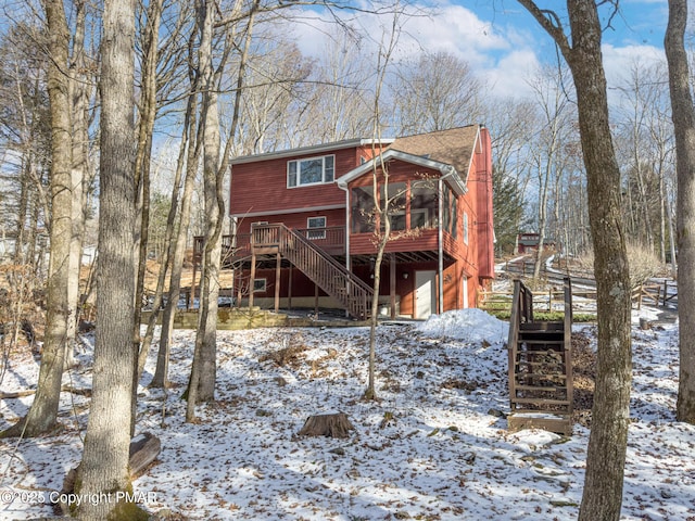 snow covered rear of property with a deck and a sunroom