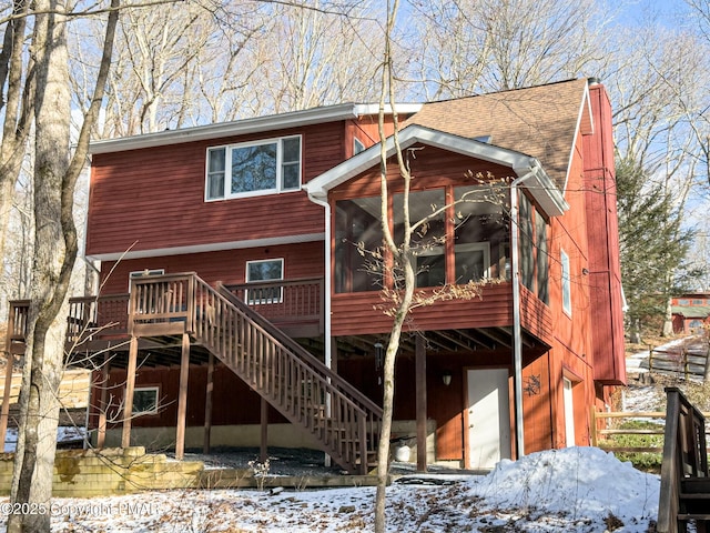 snow covered rear of property featuring a sunroom and a deck