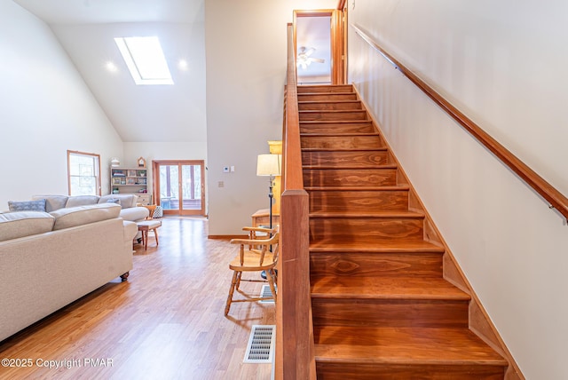 staircase with a skylight, high vaulted ceiling, and wood-type flooring