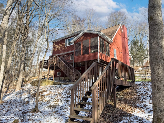 snow covered house featuring a deck and a sunroom