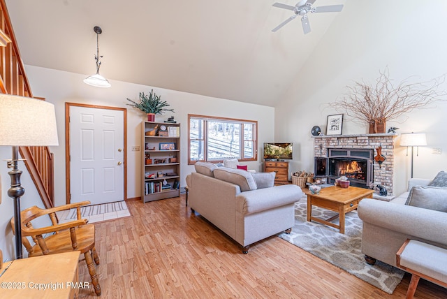 living room with ceiling fan, high vaulted ceiling, a fireplace, and light hardwood / wood-style floors