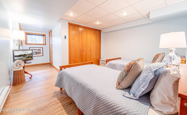 bedroom featuring a baseboard heating unit, a paneled ceiling, a closet, and light wood-type flooring