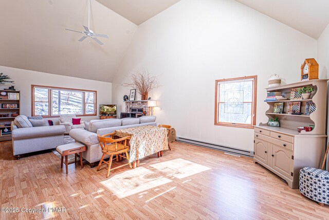 living room with high vaulted ceiling, a brick fireplace, light wood-type flooring, a baseboard radiator, and ceiling fan