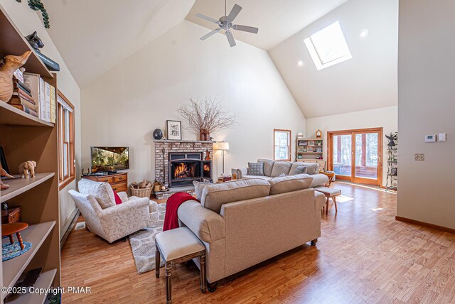 living room featuring a fireplace, a skylight, high vaulted ceiling, and light wood-type flooring