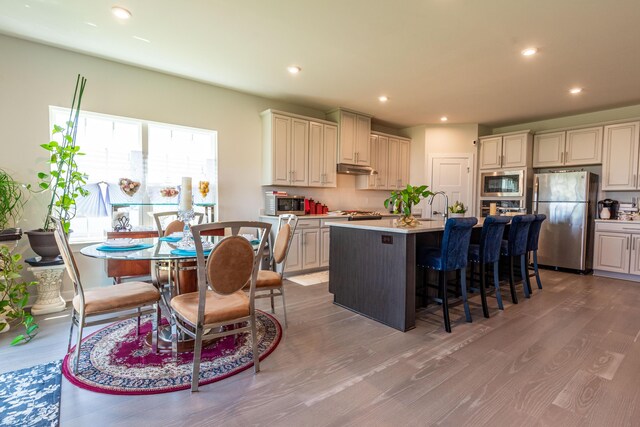 kitchen with stainless steel appliances, wood finished floors, a kitchen island with sink, a kitchen bar, and recessed lighting