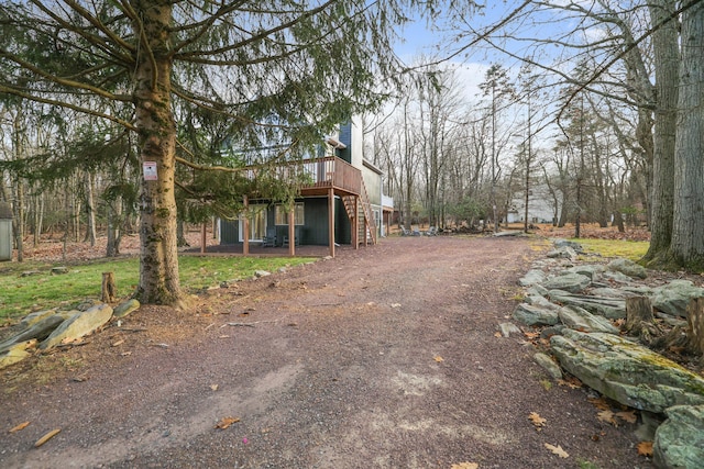 view of home's exterior with dirt driveway, a deck, and stairs