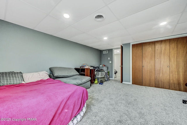 carpeted bedroom with a drop ceiling and a closet