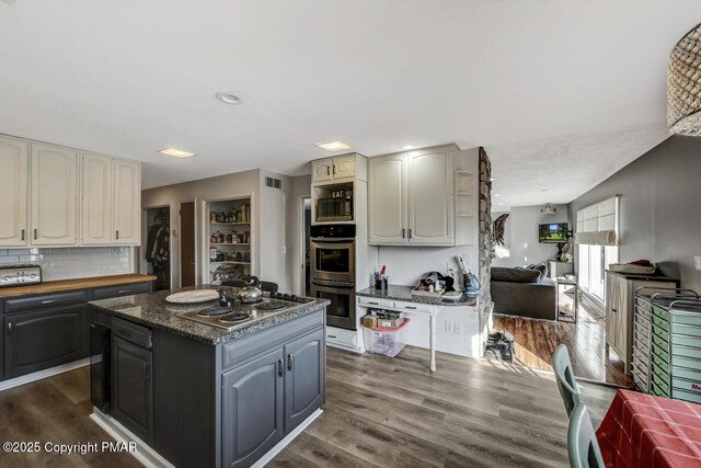 kitchen featuring tasteful backsplash, a center island, appliances with stainless steel finishes, dark hardwood / wood-style flooring, and dark stone counters