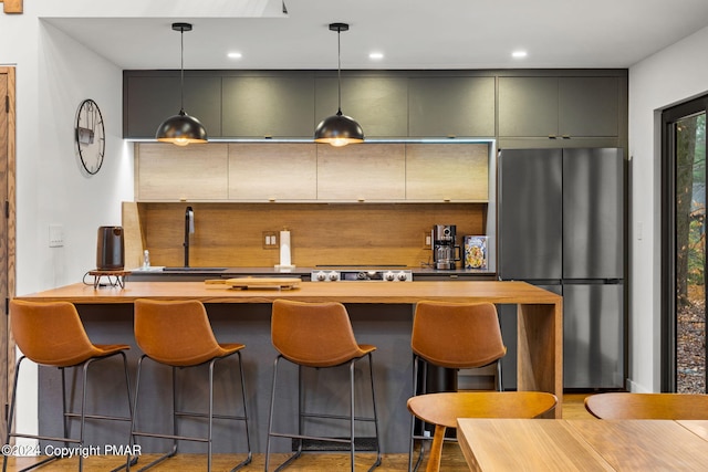 kitchen with a breakfast bar, recessed lighting, freestanding refrigerator, a sink, and pendant lighting