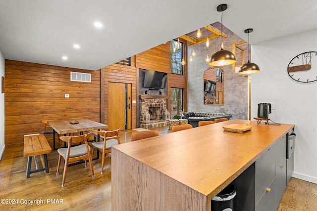 kitchen featuring wood finished floors, visible vents, a high ceiling, a fireplace, and wood walls