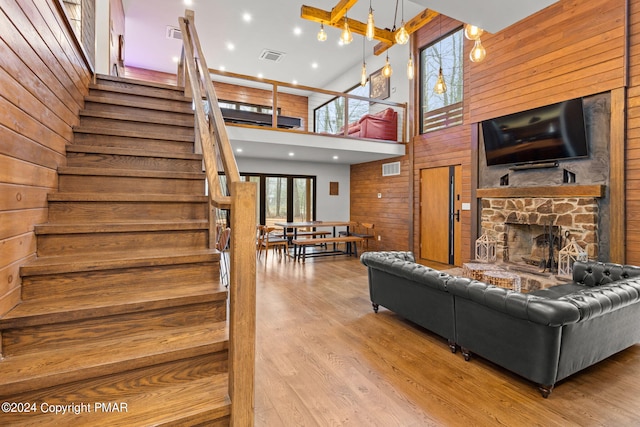 living area with visible vents, stairway, wood walls, a stone fireplace, and wood finished floors