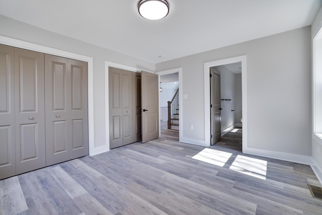 unfurnished bedroom featuring visible vents, two closets, light wood-type flooring, and baseboards