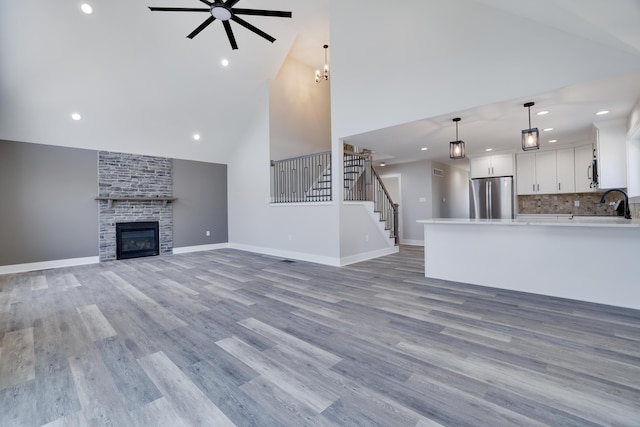 unfurnished living room featuring a ceiling fan, a large fireplace, light wood finished floors, baseboards, and stairs