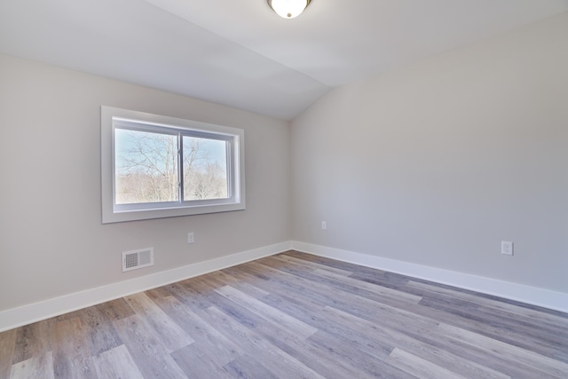 unfurnished room with wood finished floors, baseboards, visible vents, and lofted ceiling