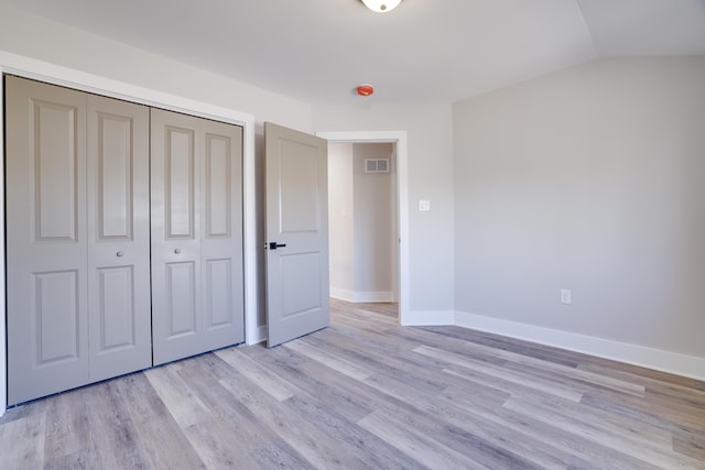 unfurnished bedroom with visible vents, lofted ceiling, light wood-style flooring, a closet, and baseboards