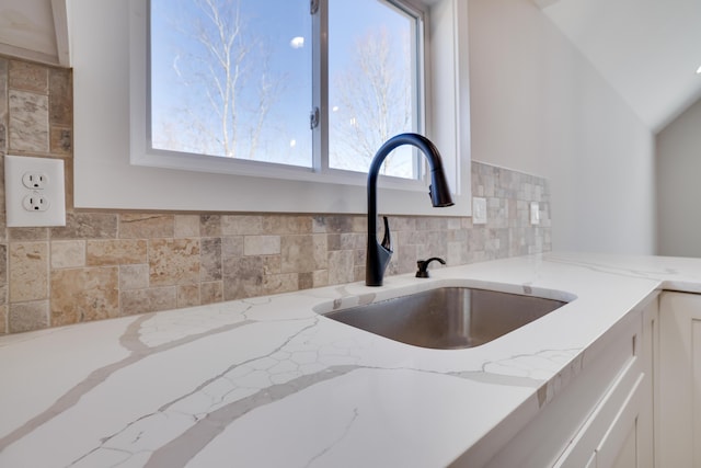 details with light stone counters, backsplash, white cabinetry, and a sink