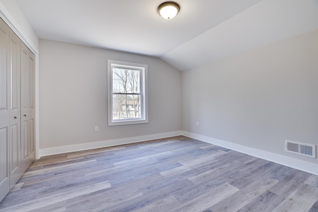 unfurnished bedroom with visible vents, lofted ceiling, light wood-style flooring, a closet, and baseboards