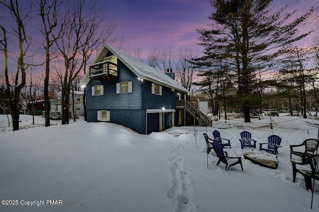 view of snowy exterior featuring an attached garage, a chimney, stairs, and a balcony