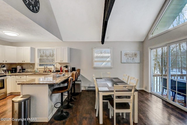 kitchen with sink, baseboard heating, a kitchen breakfast bar, light stone counters, and white cabinets