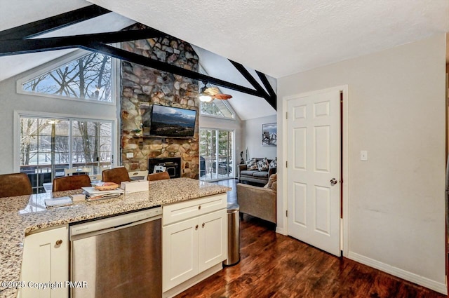 kitchen with dark wood-type flooring, vaulted ceiling with beams, stainless steel dishwasher, a fireplace, and light stone countertops