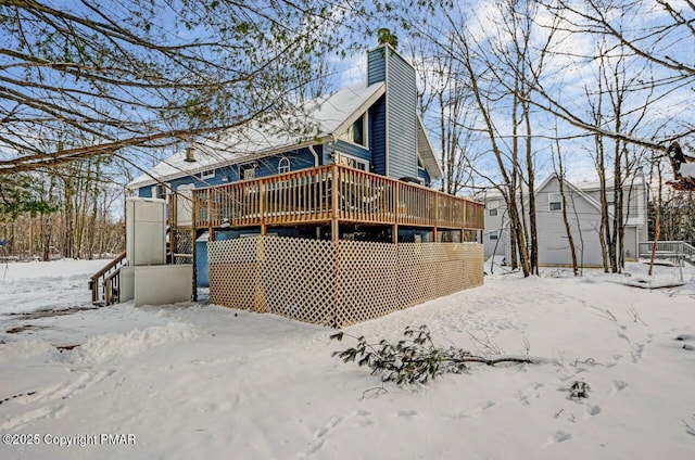 snow covered house with a wooden deck and a chimney