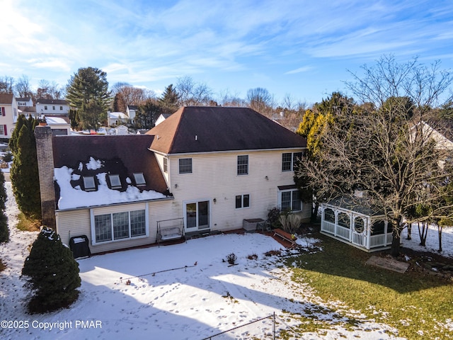 snow covered back of property featuring a chimney