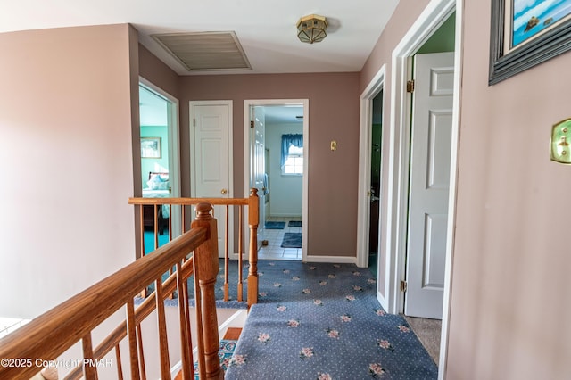 hallway featuring baseboards, visible vents, carpet flooring, and an upstairs landing