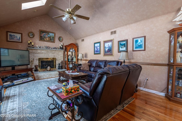 living area with a skylight, visible vents, a ceiling fan, wood finished floors, and a fireplace