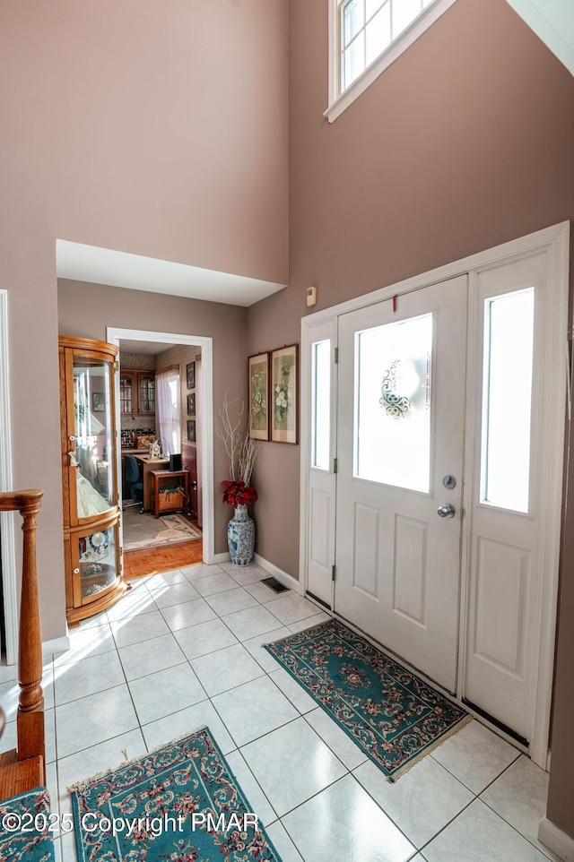 foyer entrance featuring a towering ceiling, light tile patterned floors, and baseboards