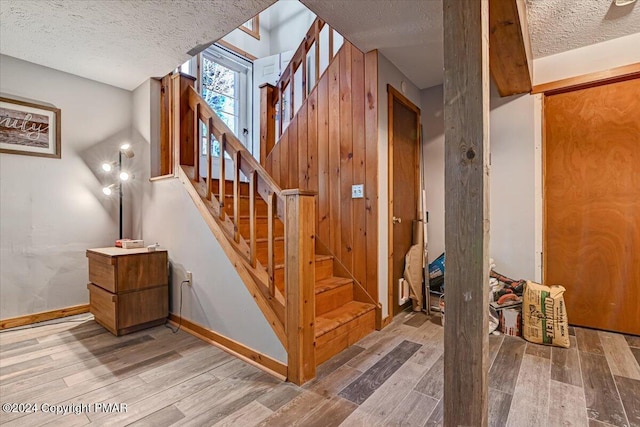 staircase featuring a textured ceiling, baseboards, and wood finished floors