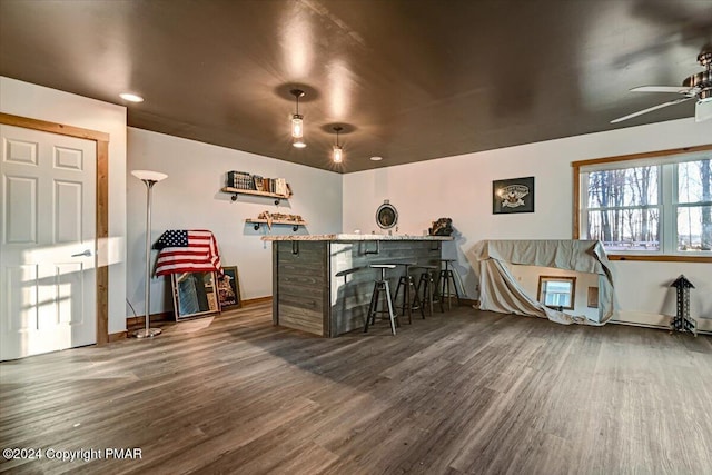 bar featuring dark wood-style floors, ceiling fan, a bar, and baseboards