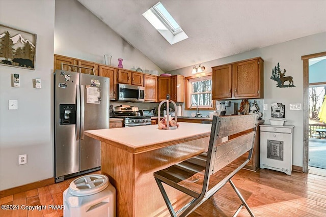 kitchen featuring a breakfast bar, brown cabinets, light wood-style flooring, appliances with stainless steel finishes, and lofted ceiling with skylight