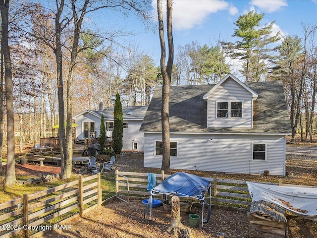 back of property with a shingled roof, fence, and a deck