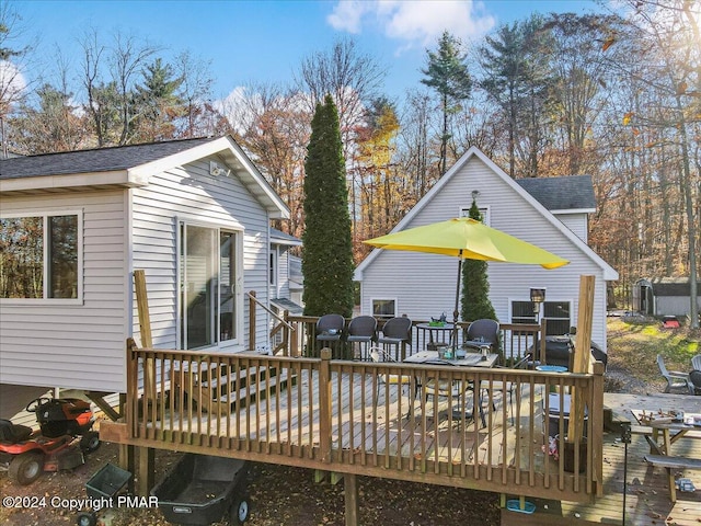 back of property with outdoor dining area, roof with shingles, and a deck