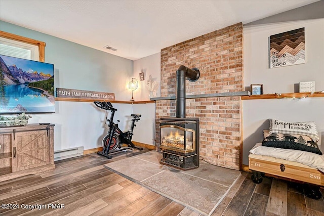 living area featuring a baseboard radiator, a wood stove, visible vents, and wood finished floors